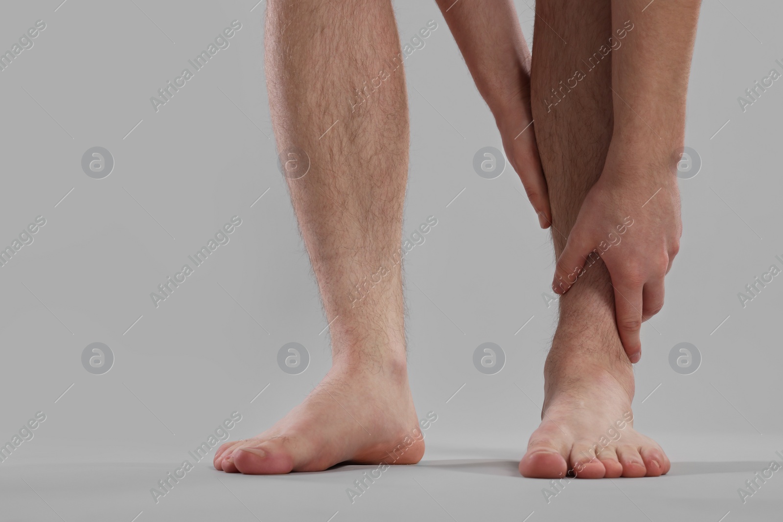 Photo of Man suffering from leg pain on grey background, closeup