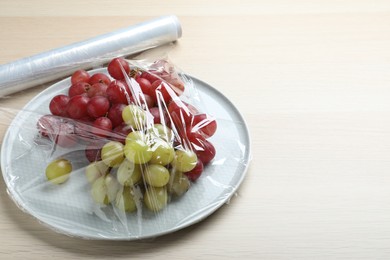 Photo of Plate of fresh grapes with plastic food wrap on wooden table. Space for text