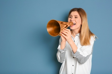 Young woman shouting into megaphone on color background