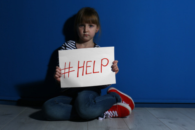 Photo of Abused little girl with hashtag HELP near blue wall. Domestic violence concept