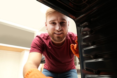 Photo of Young man cleaning oven in kitchen, view from inside