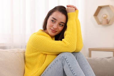 Photo of Beautiful young woman in stylish warm sweater on sofa at home