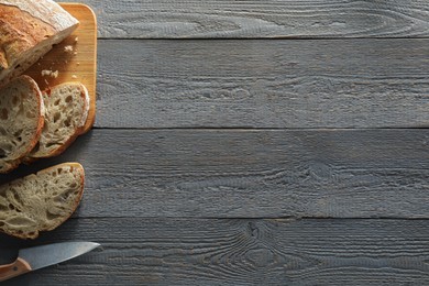 Photo of Food photography. Cut freshly baked bread and knife on wooden table, flat lay with space for text