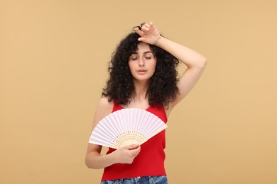 Photo of Woman with hand fan suffering from heat on beige background