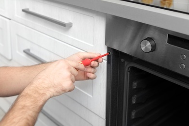 Photo of Professional serviceman repairing modern oven in kitchen, closeup