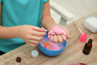Photo of Little girl making DIY slime toy at table indoors, closeup