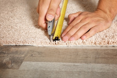 Photo of Man cutting new carpet flooring indoors, closeup. Space for text