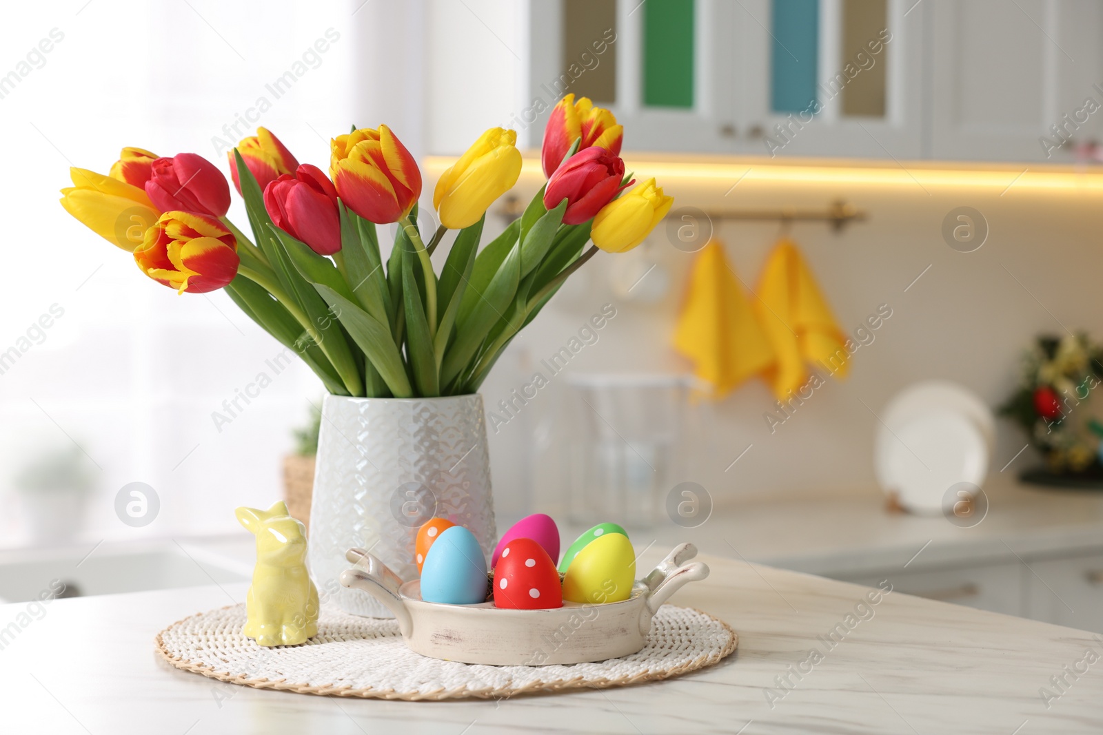 Photo of Easter decorations. Bouquet of tulips, painted eggs and bunny figure on table indoors. Space for text