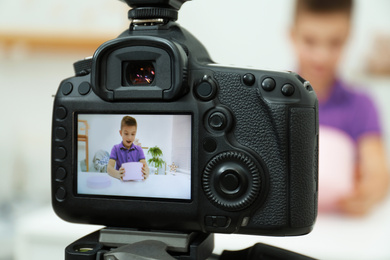 Photo of Emotional little blogger with box recording video at home, focus on camera