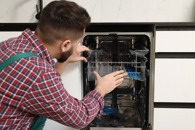 Photo of Serviceman repairing dishwasher cutlery rack indoors, closeup