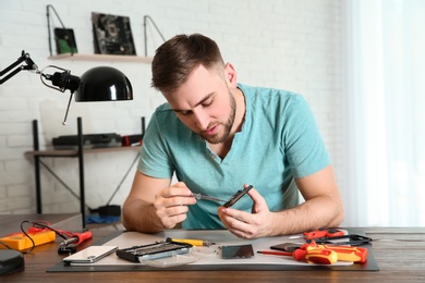 Technician repairing mobile phone at table in workshop