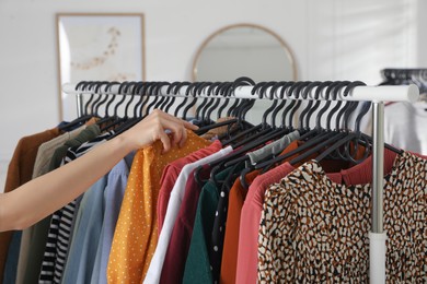 Photo of Woman picking clothes from rack indoors, closeup. Fast fashion