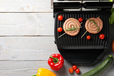Photo of Electric grill with homemade sausages, rosemary and vegetables on rustic wooden table, flat lay. Space for text