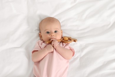 Photo of Cute little baby with toy on white sheets, top view
