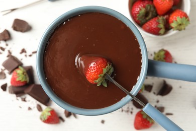Photo of Dipping strawberry into fondue pot with chocolate on white table, top view