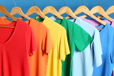Photo of Bright clothes on wooden hangers against blue background. Rainbow colors