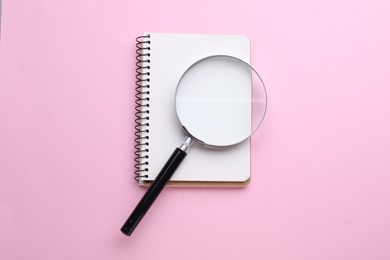 Photo of Magnifying glass and notebook on pink background, top view