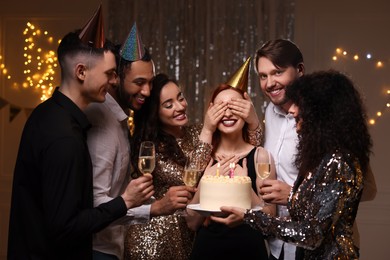 Photo of Happy friends with tasty cake and glasses of sparkling wine celebrating birthday indoors