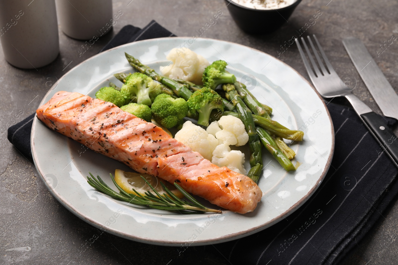 Photo of Healthy meal. Piece of grilled salmon, vegetables, asparagus and rosemary served on grey textured table, closeup