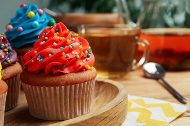 Photo of Delicious cupcakes with colorful cream and sprinkles on wooden board, closeup. Space for text