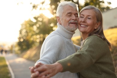 Photo of Affectionate senior couple dancing together outdoors at sunset, space for text