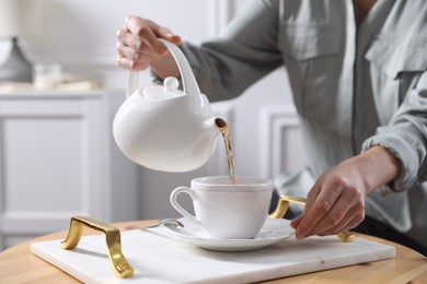 Photo of Woman pouring hot tea into cup at wooden table, closeup