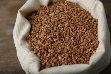 Photo of Uncooked buckwheat in sackcloth bag on table, closeup