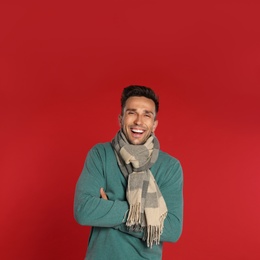 Photo of Happy young man in scarf and sweatshirt on red background. Winter season