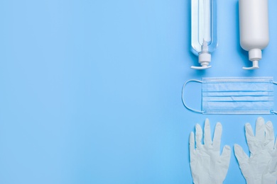 Photo of Medical gloves, mask and hand sanitizers on light blue background, flat lay. Space for text