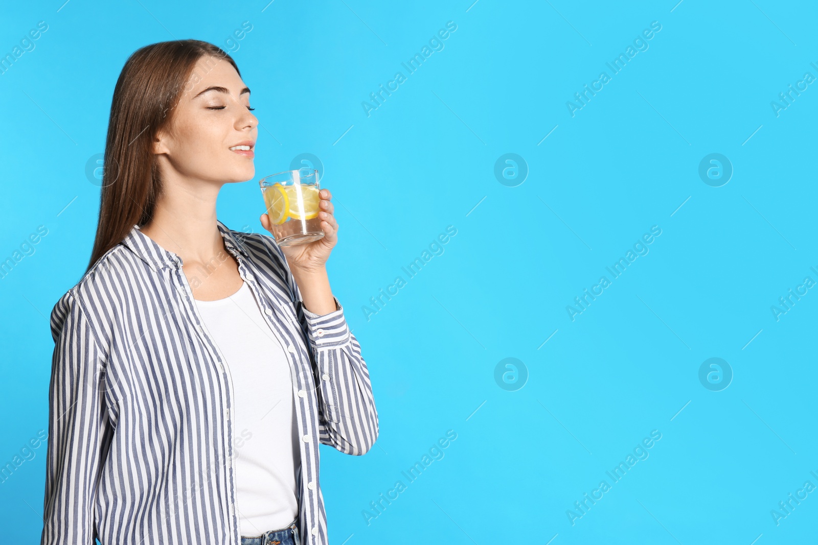 Photo of Young woman with glass of lemon water on light blue background. Space for text
