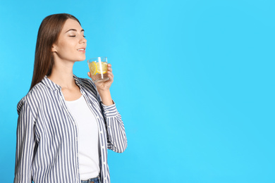 Photo of Young woman with glass of lemon water on light blue background. Space for text