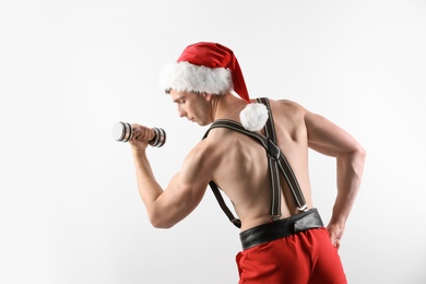 Photo of Young muscular man in Santa hat with dumbbell on white background