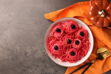 Photo of Red pasta with olives in bowl on grey textured table, flat lay with space for text. Halloween food