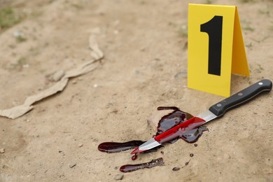 Crime scene marker and bloody knife on ground outdoors. Space for text