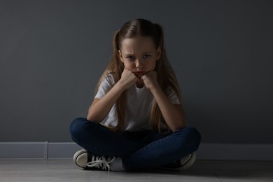 Photo of Sad girl sitting on floor near dark grey wall indoors