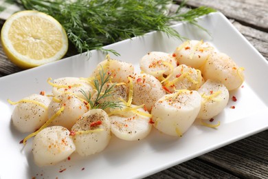Photo of Raw scallops with spices, dill and lemon zest on wooden table, closeup