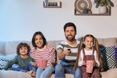 Photo of Happy family watching TV with popcorn on sofa indoors
