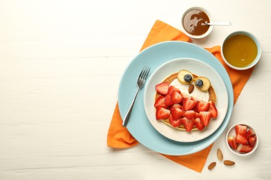 Photo of Creative serving for kids. Plate with cute owl made of pancakes, strawberries, cream, banana and almond on white wooden table, flat lay. Space for text