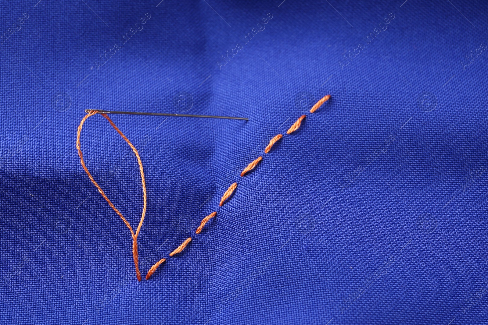 Photo of Sewing needle with thread and stitches on blue cloth, above view