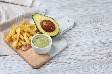 Photo of Serving board with french fries, guacamole dip and avocado on white wooden table, space for text