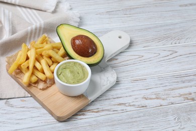 Photo of Serving board with french fries, guacamole dip and avocado on white wooden table, space for text
