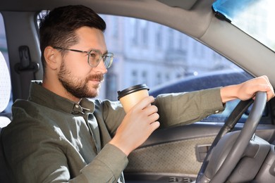 Photo of Coffee to go. Handsome man with paper cup of drink driving his car