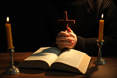 Woman praying at table with burning candles and Bible, closeup