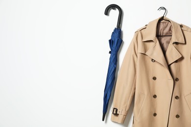 Photo of Hanger with beige trench coat and blue umbrella on white wall, space for text