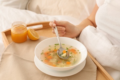 Photo of Sick woman eating fresh homemade soup to cure flu in bed at home, closeup
