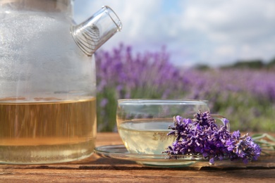 Photo of Tasty herbal tea and fresh lavender flowers on wooden table in field, closeup