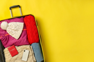 Photo of Open suitcase with warm clothes, passport and smartphone on color background, top view. Space for text