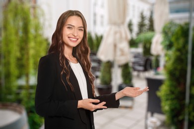 Image of Portrait of hostess in uniform and blurred view of cafe on sunny day. Space for text