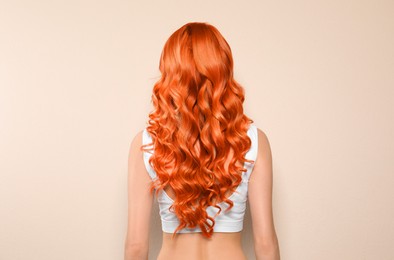 Beautiful woman with long orange hair on beige background, back view
