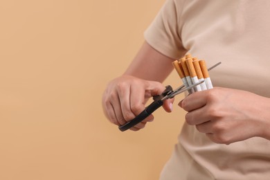 Photo of Stop smoking concept. Woman cutting cigarettes on light brown background, closeup. Space for text
